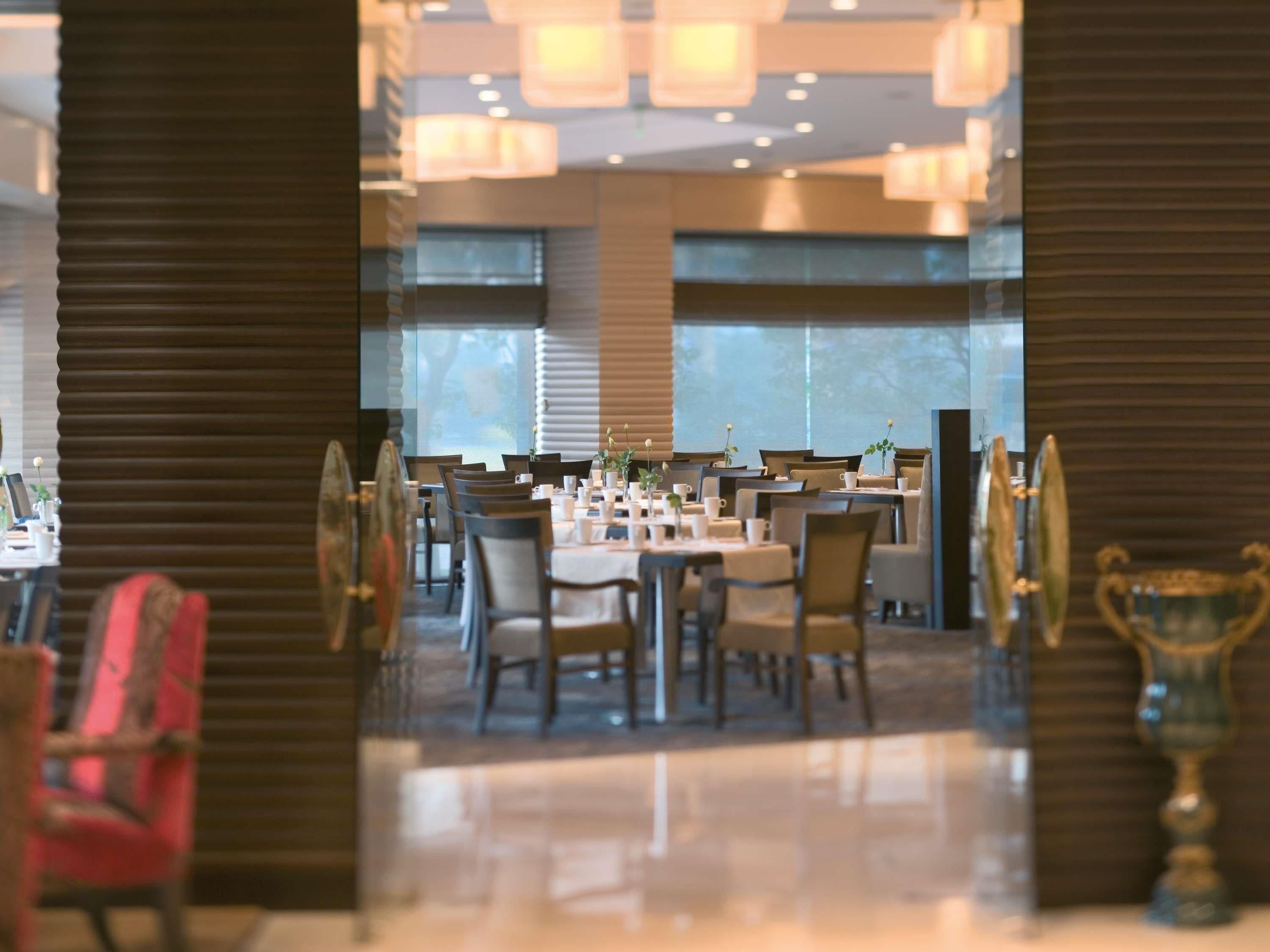 Un comedor amplio con varias mesas y sillas, ventanas grandes y lámparas modernas.