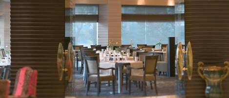 Un comedor amplio con varias mesas y sillas, ventanas grandes y lámparas modernas.