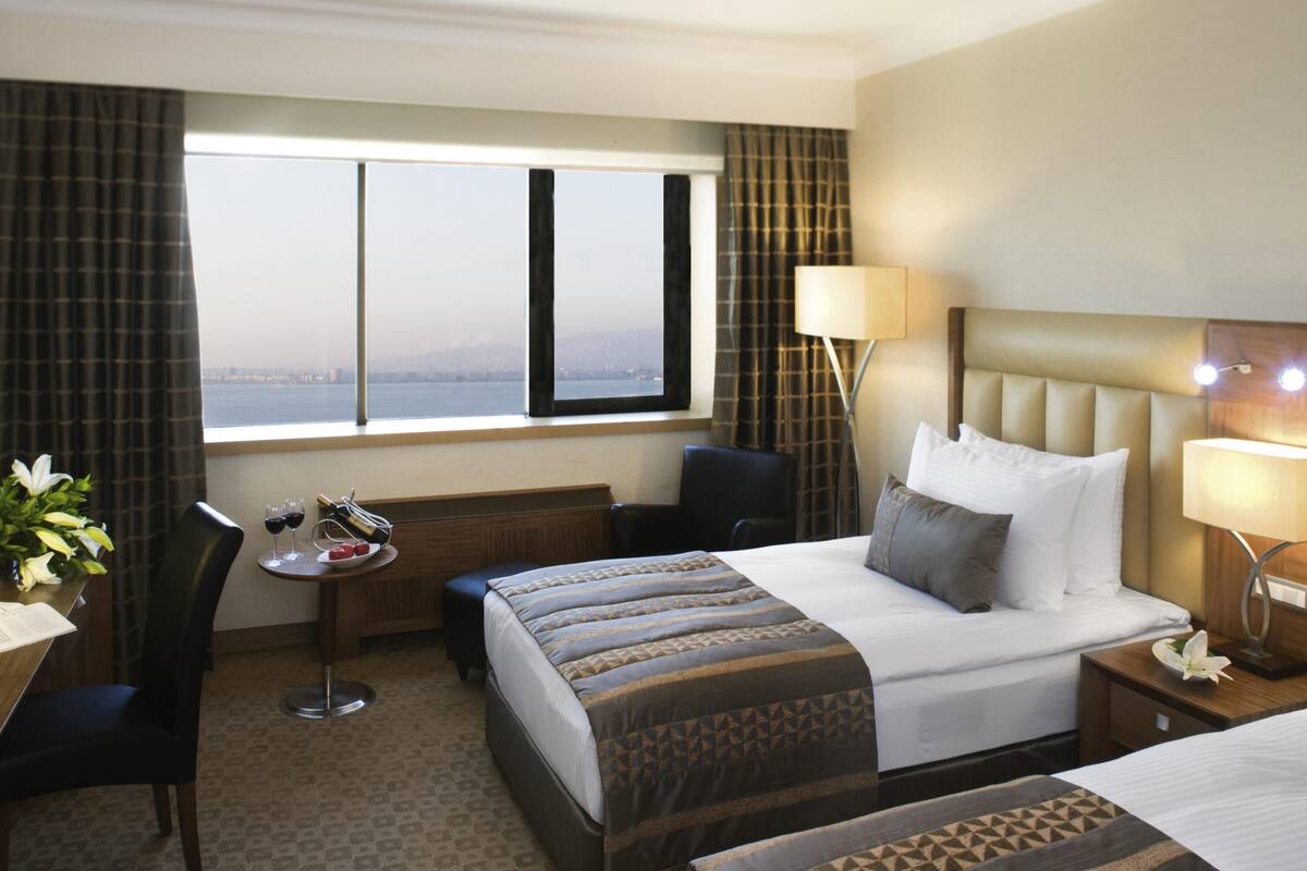 Habitación de hotel con una cama grande, un escritorio, una silla y vista a la ciudad desde la ventana.