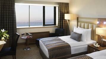 Habitación de hotel con una cama grande, un escritorio, una silla y vista a la ciudad desde la ventana.