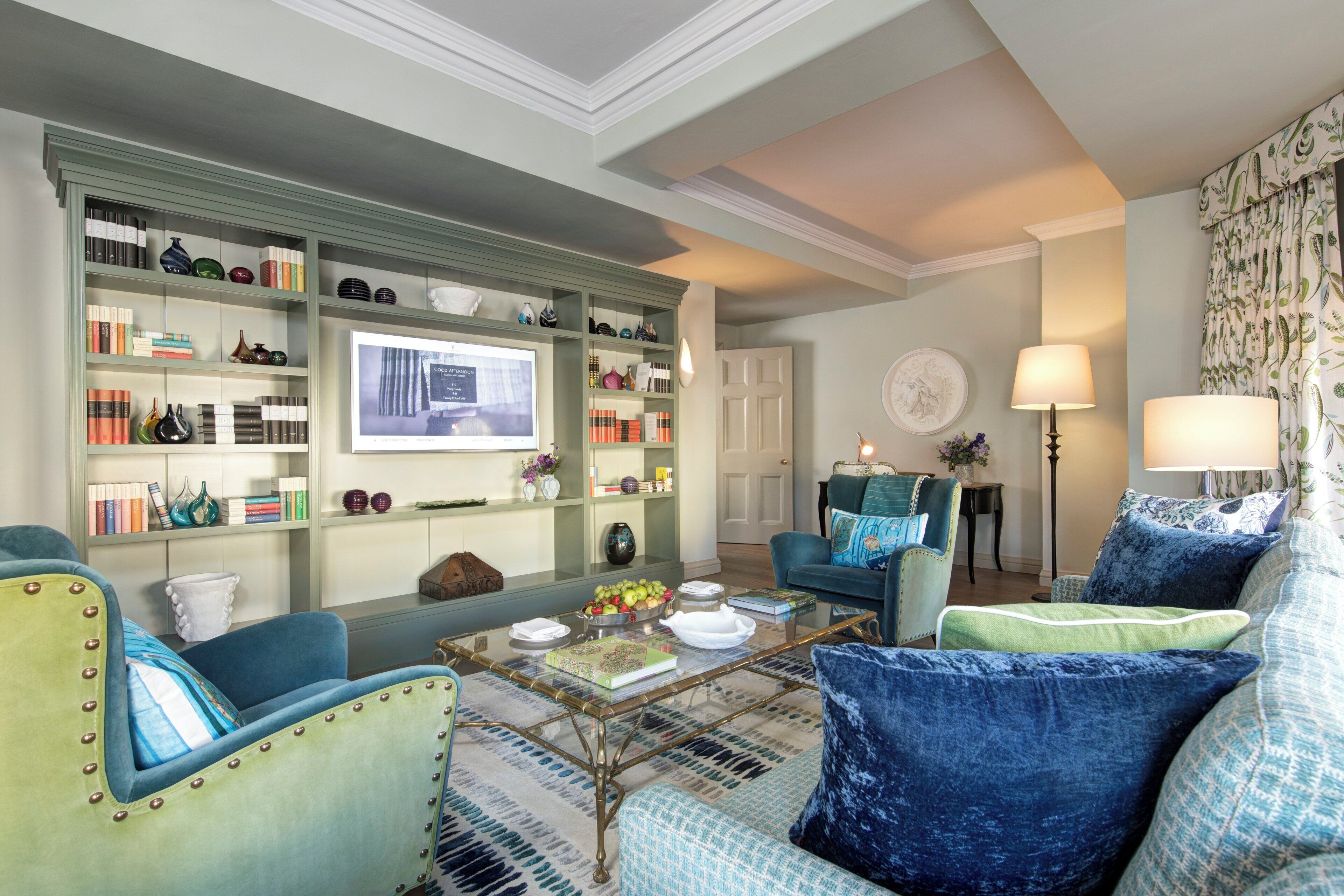 A well-lit living room with a bookshelf, a coffee table with books and decorative items, a blue armchair, and a sofa with blue cushions.