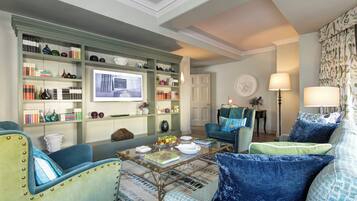 A well-lit living room with a bookshelf, a coffee table with books and decorative items, a blue armchair, and a sofa with blue cushions.
