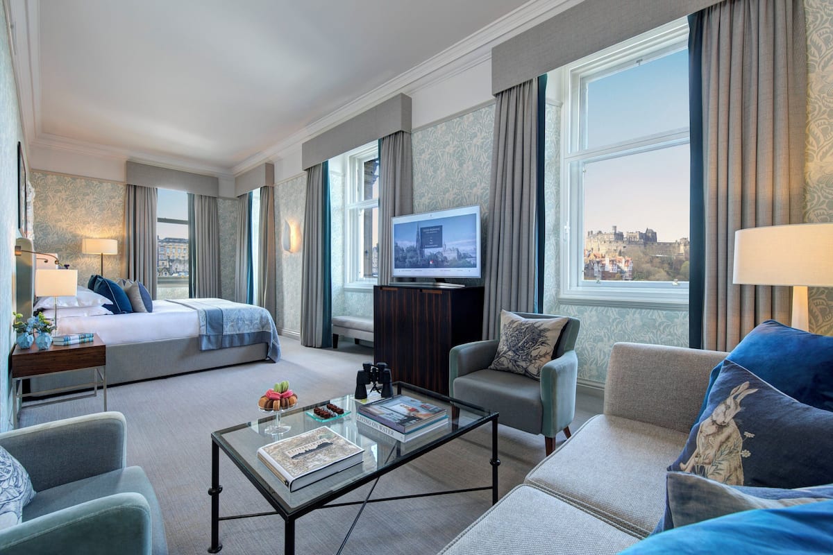Camera d'albergo con un letto, una poltrona, un tavolino, una TV e vista sulla città.
