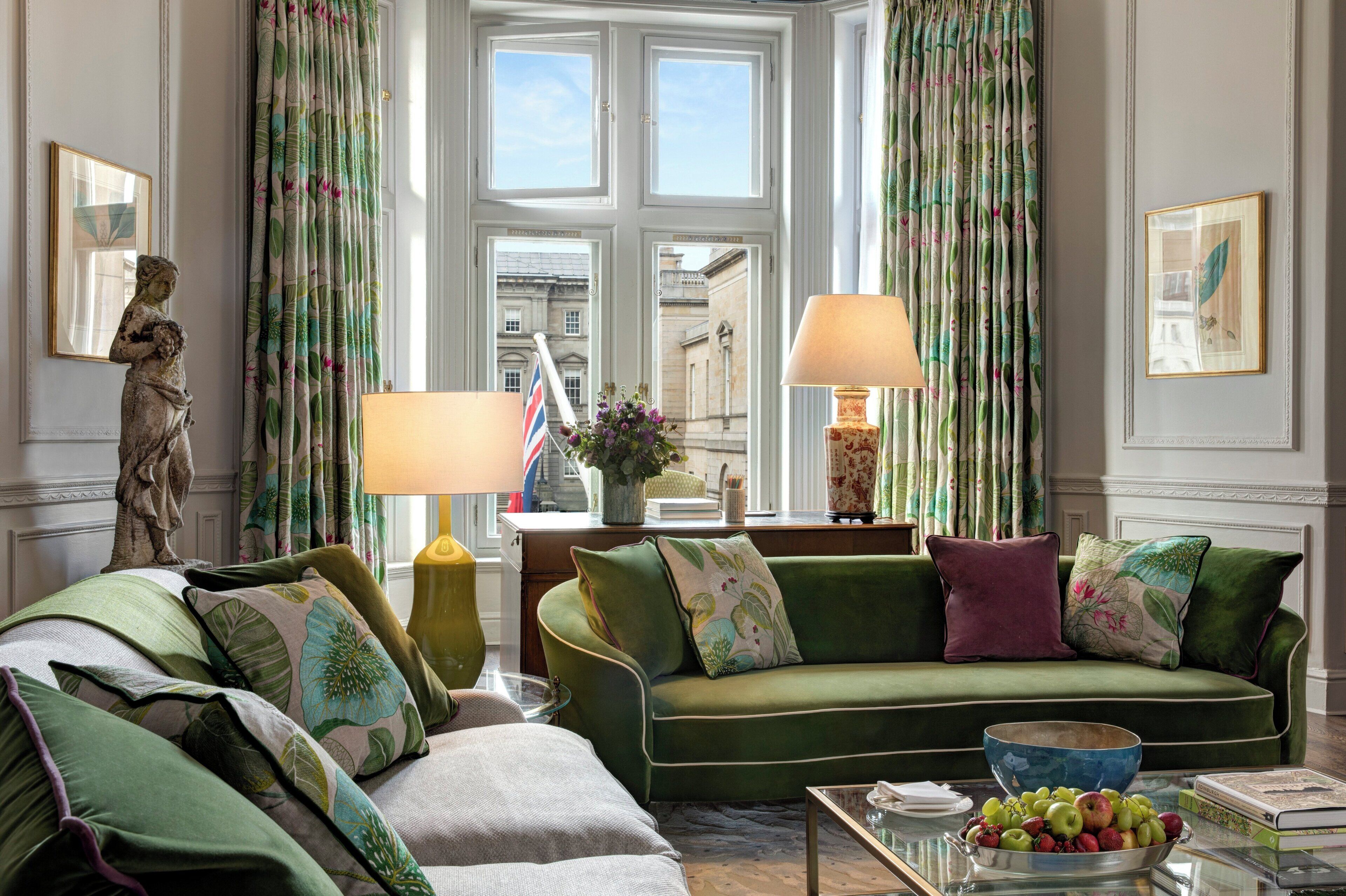 A well-appointed living room with a green sofa, a statue, and a view of a building through the windows.