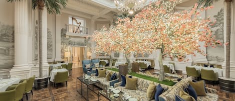 A grand dining room with a high ceiling, ornate columns, and a large floral arrangement.