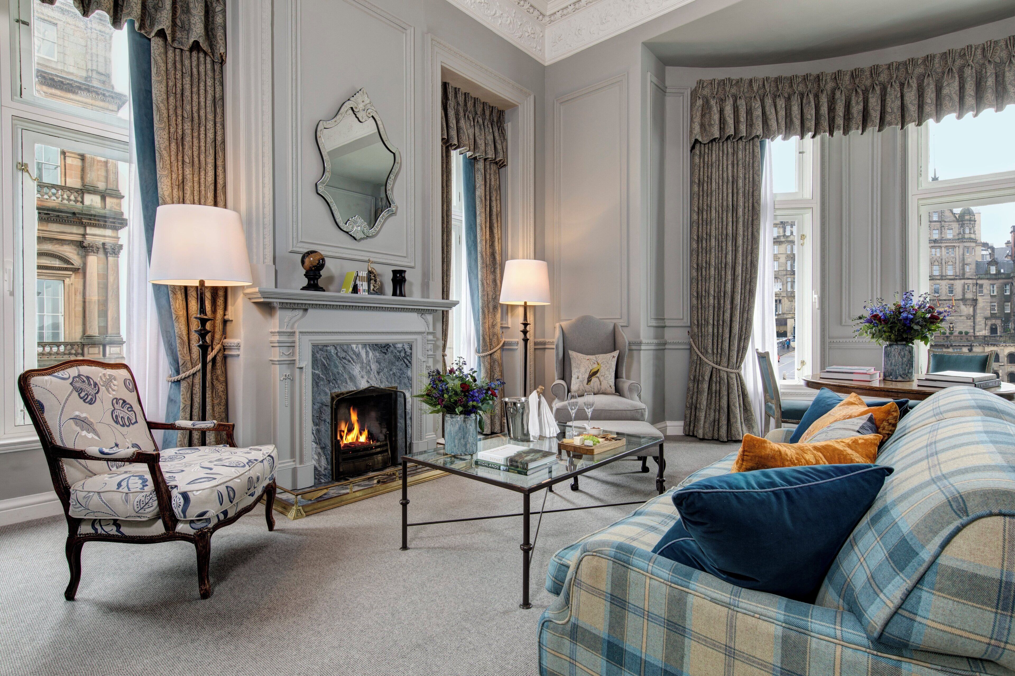 A room with a fireplace, a sofa, a chair, and a table with a vase of flowers.