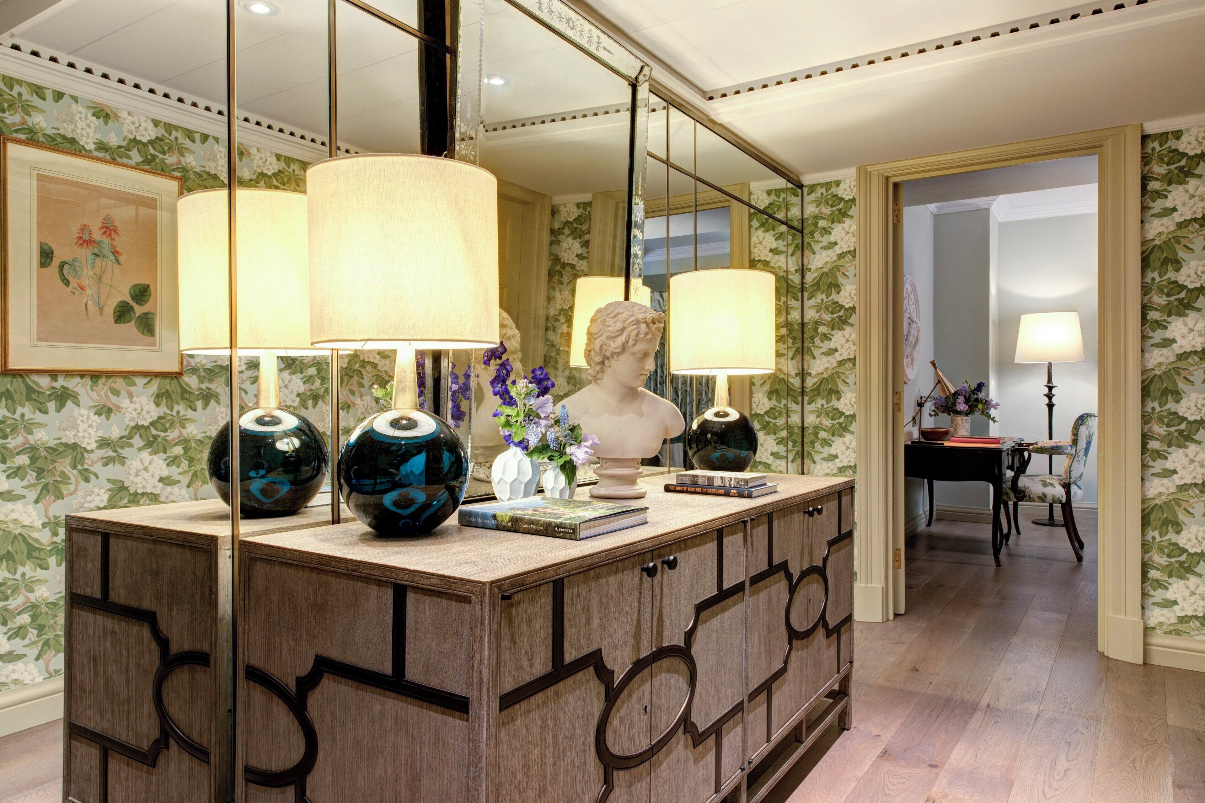 A well-lit room with a wooden cabinet, two lamps, a bust sculpture, and a vase with flowers.
