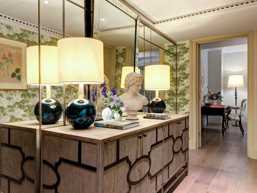 A well-lit room with a wooden cabinet, two lamps, a bust sculpture, and a vase with flowers.