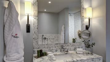 A modern bathroom with a marble sink, two wall-mounted lamps, a large mirror, and a towel rack with a branded towel.