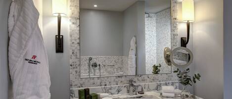 Une salle de bain moderne avec un lavabo en marbre, deux lampes fixées au mur, un grand miroir et un porte-serviettes agrémenté d’une serviette de marque.