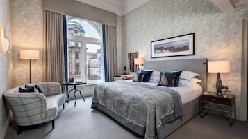 Habitación de hotel con una cama grande, un sofá, una mesita y una ventana con vistas a edificios.