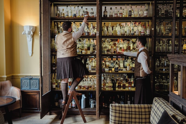 Baarialue, jossa on hyllyjä täynnä alkoholijuomapulloja, puiset tikkaat ja baaritiski.