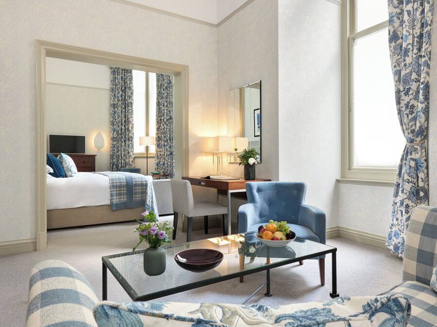 Ein Hotelzimmer mit Bett, Schreibtisch, Stuhl, Sofa, Couchtisch und einem Fenster mit Vorhängen.