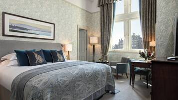 Ein Hotelzimmer mit einem großen Bett, einem Schreibtisch, einem Stuhl und Blick auf die Stadt durch das Fenster.