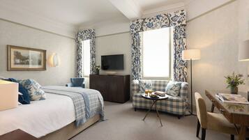 A hotel room with a bed, a sofa, a small table with drinks, a TV, and a desk with a lamp.