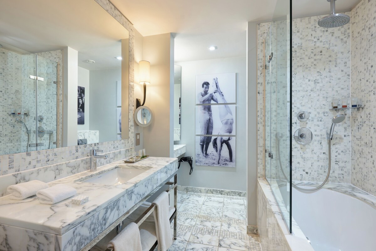Un bagno moderno con un vanità in marmo, uno specchio grande, un box doccia in vetro e un water sospeso.