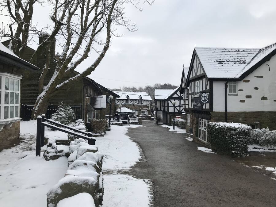 A narrow snow-covered street in a traditional village with stone buildings and a pub.