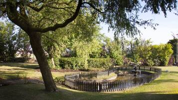 A park with a circular pond, a wooden fence, and a large tree.
