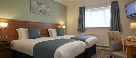 A hotel room with two beds, a headboard, a painting, a window with curtains, a chair, and a desk with a lamp.
