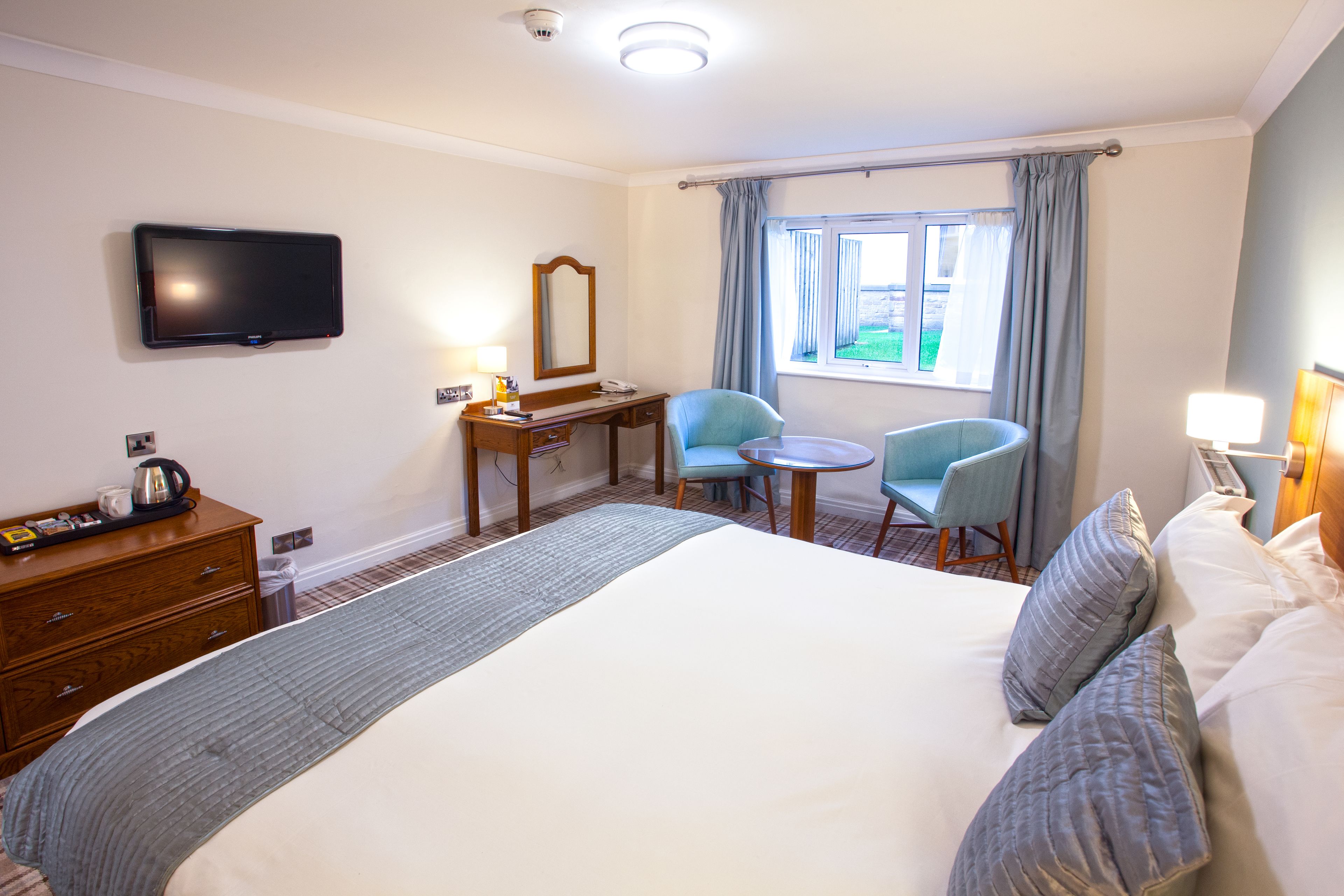 A hotel room with a large bed, a desk, two chairs, a television, and a window with curtains.