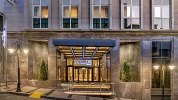 A hotel entrance with a glass door, a sign above the entrance, and two potted plants on either side.