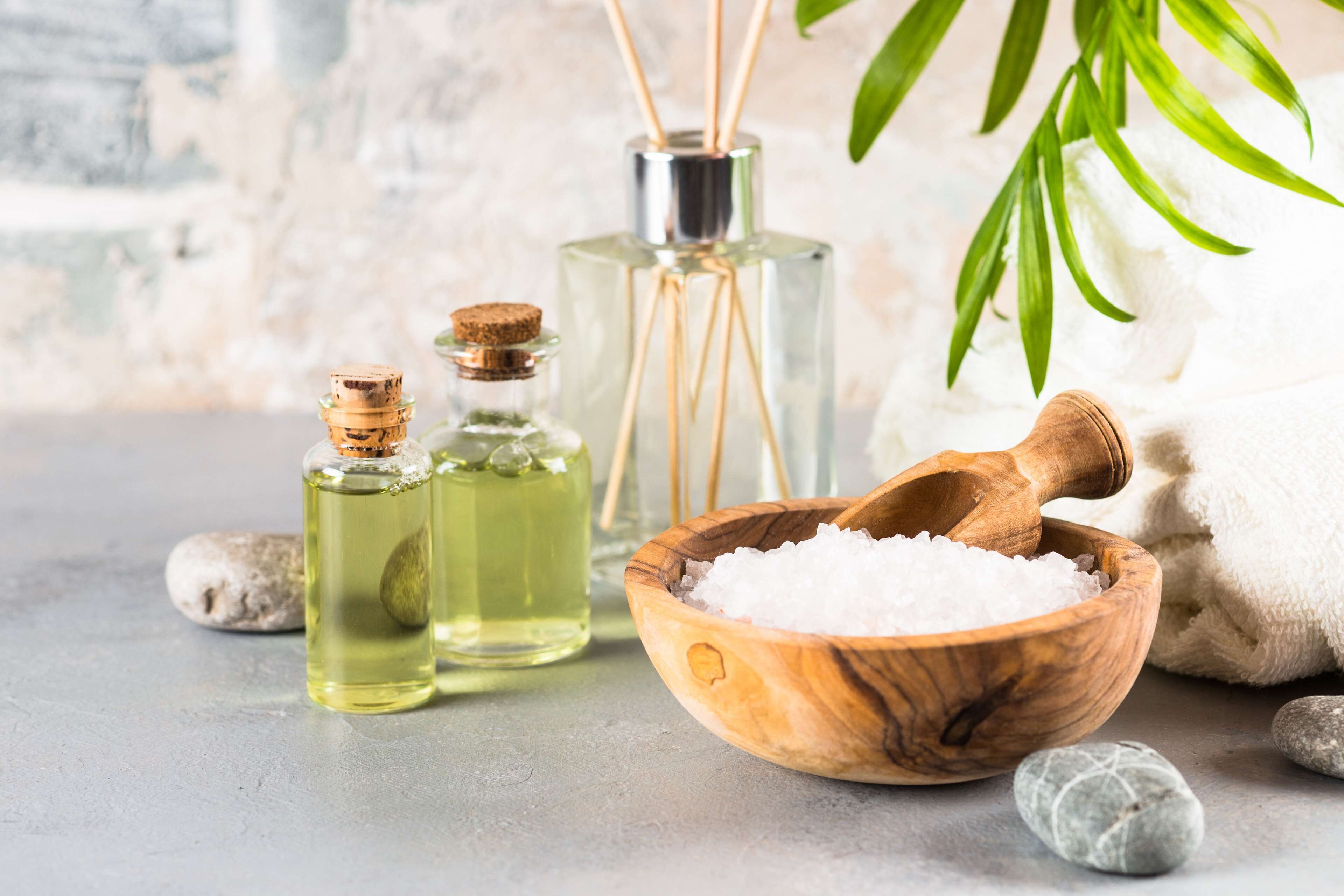 Un bol en bois rempli de sels de bain blancs, deux bouteilles en verre munies de bouchons en liège et une serviette blanche.