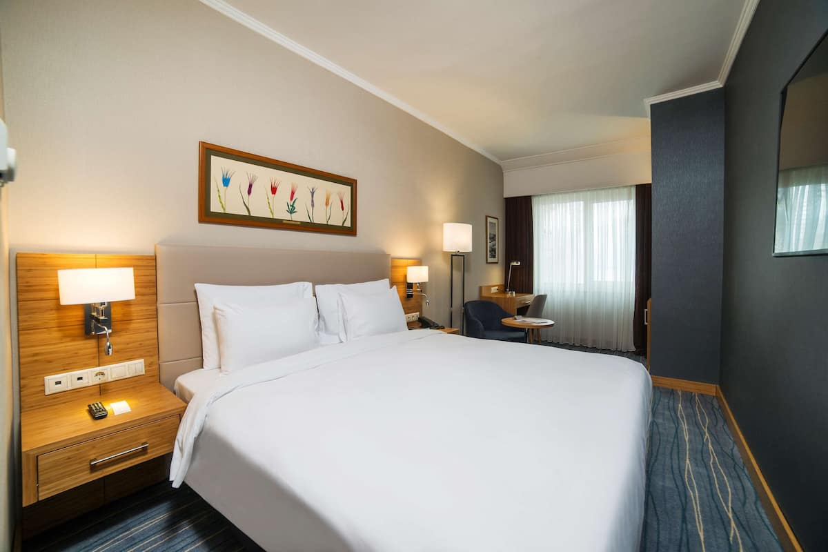 Una habitación de hotel con una cama grande, mesitas de noche con lámparas, un escritorio y una silla.