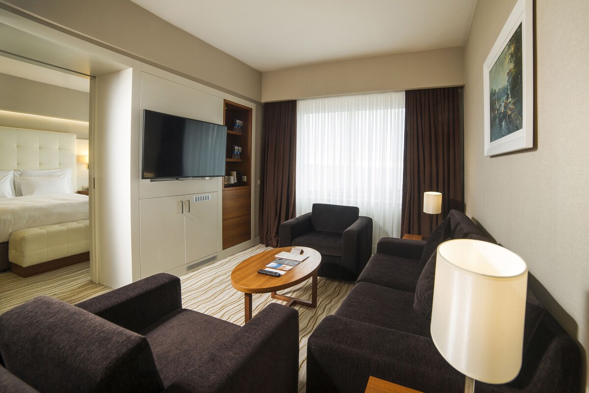 A hotel room with a bed, a TV, a sofa, a coffee table, and a desk.