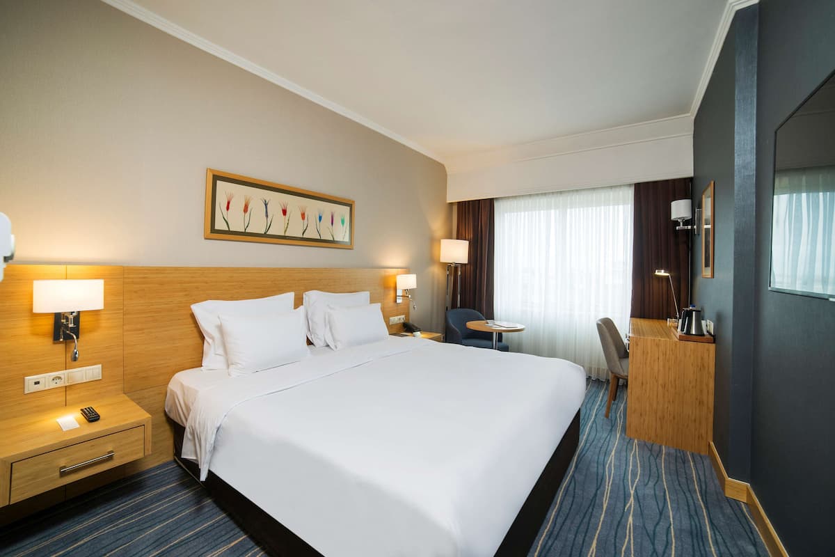Una habitación de hotel con una cama grande, mesitas de noche, un escritorio y una silla.