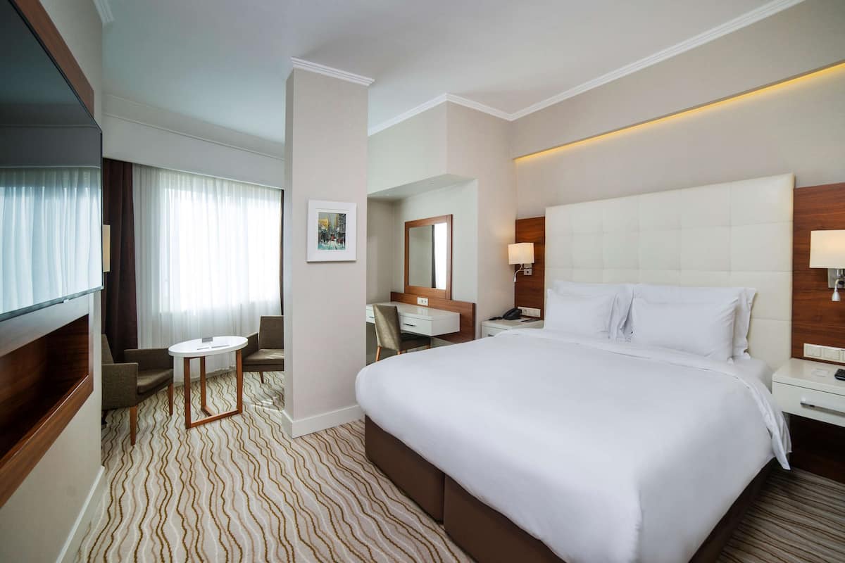 Una habitación de hotel con una cama grande, un escritorio, una silla, una mesita y un televisor.