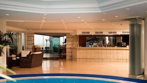 Eine Hotlellobby mit Schwimmbad, Barbereich und einer Sitzecke mit Rattan-Sofa.