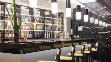 Un espace bar doté d’un comptoir en marbre, d’étagères remplies de bouteilles d’alcool, de luminaires suspendus et de tabourets de bar.