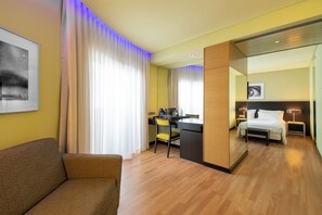 A hotel room with a sofa, a desk with a chair, a bed with a nightstand, and a mirror. - SANA Capitol Hotel (Lisbon)