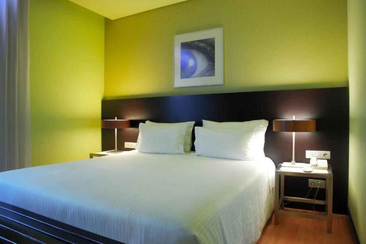 A hotel room with a large bed, two bedside tables with lamps, a wall-mounted artwork, and a nightstand with a phone.