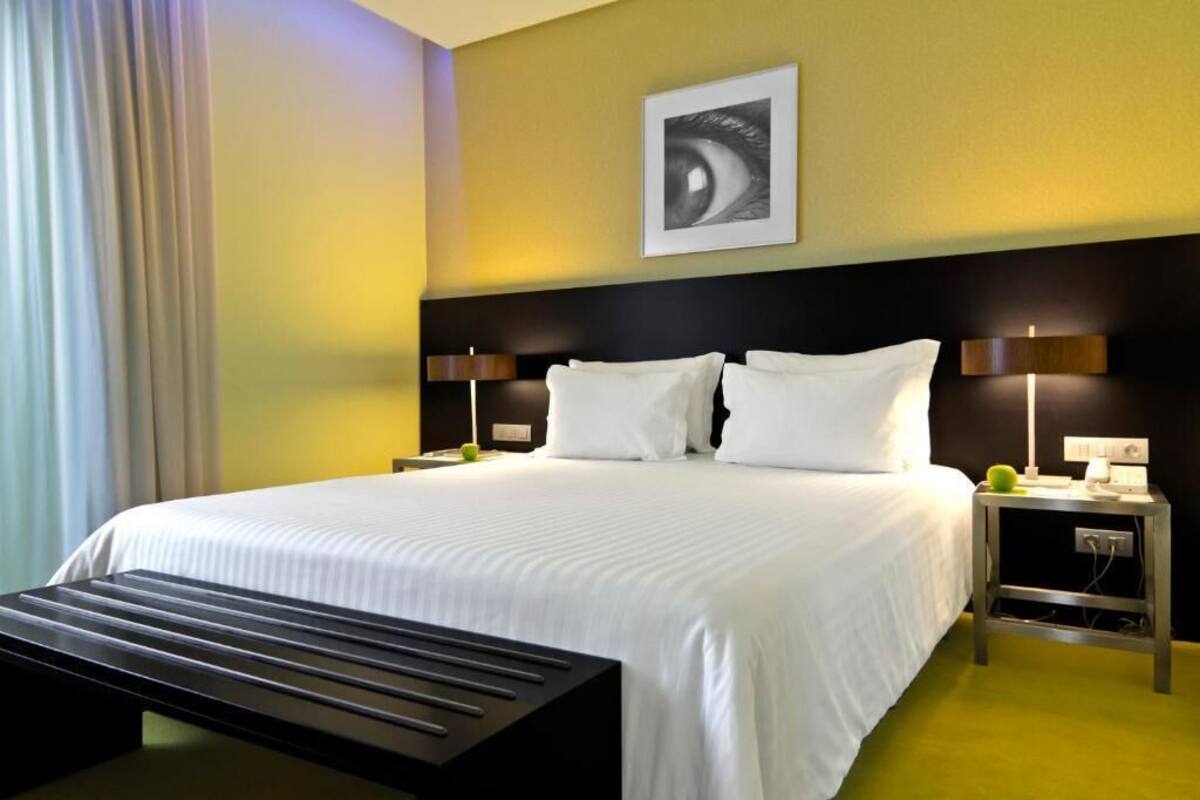 A hotel room with a large bed, two bedside tables, a wall-mounted lamp, and a framed picture.