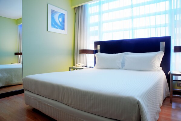 A hotel room with a large bed, a bedside table with a lamp, a framed picture on the wall, and a window with curtains. - SANA Capitol Hotel (Lisbon)