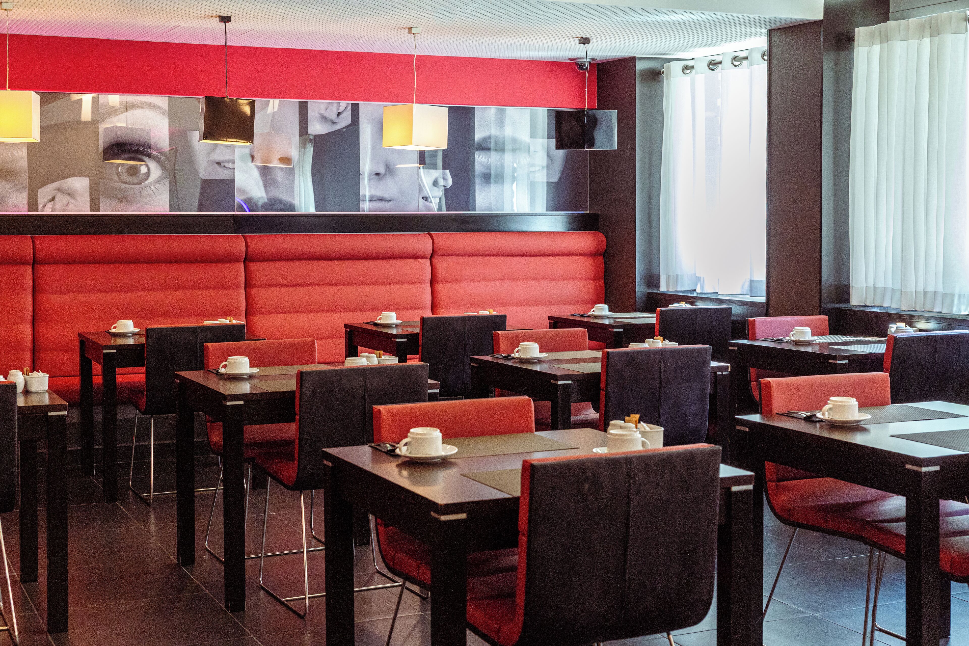 A restaurant with red booths and black tables, featuring a modern interior design and large windows.
