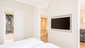 A hotel room with a bed, a TV mounted on the wall, and a view of a cityscape through a glass door.