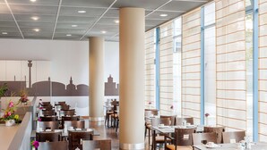 A spacious dining area with high ceilings, large windows, and modern furnishings. - NH Dortmund (Dortmund)