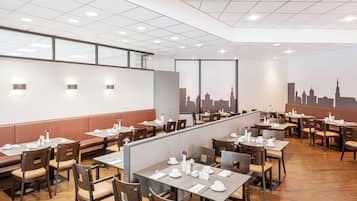 Ein modernes Restaurant mit hohen Tischen und Sitzecken, Wandgemälde mit Stadtansicht und viel Tageslicht.