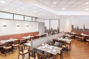 A modern restaurant with high tables and booths, city skyline mural, and ample natural light.