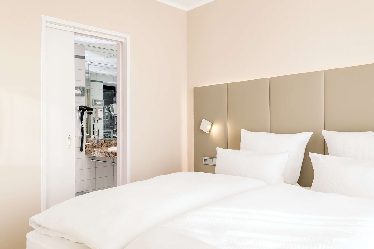 A neatly made bed with white linens in a hotel room.