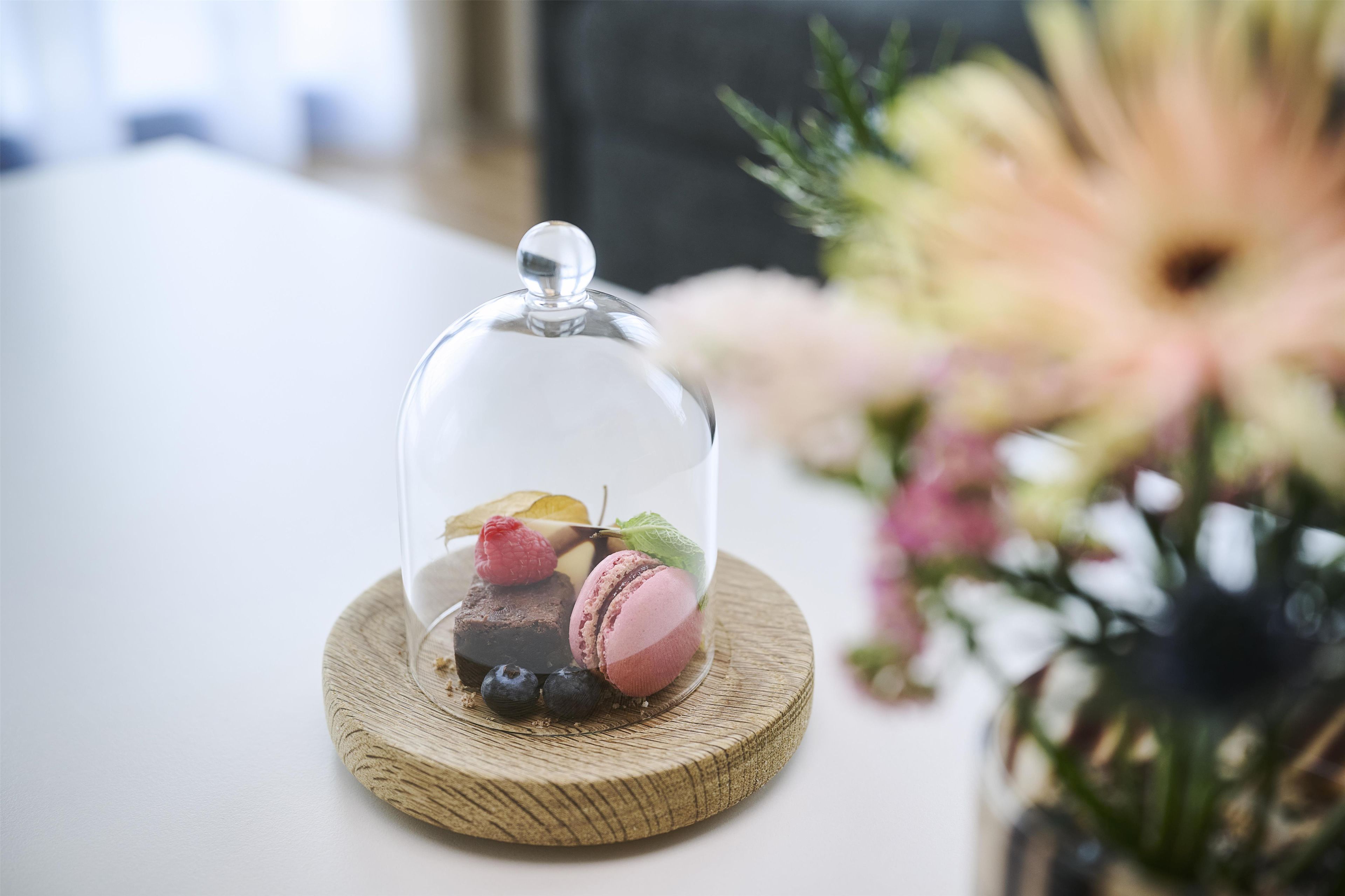 A dessert under a glass dome on a wooden coaster.