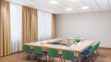 Ein Konferenzraum mit einem langen Tisch, grünen und blauen Stühlen und einem Teppichboden.
