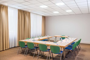 A conference room with a long table, green and blue chairs, and a carpeted floor. - NH Dortmund (Dortmund)