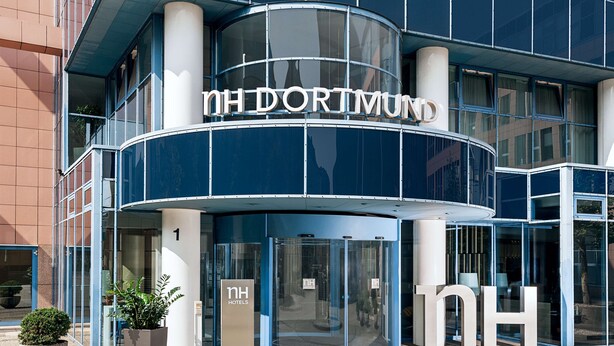 A modern hotel entrance with a curved facade, large glass doors, and a prominent 'nh hotels' sign. - NH Dortmund (Dortmund)