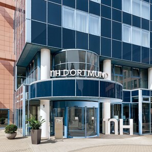 A modern hotel entrance with a curved facade, large glass doors, and a prominent 'nh hotels' sign. - NH Dortmund (Dortmund)