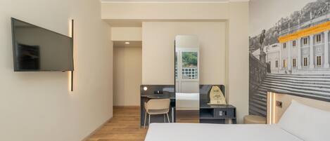 A hotel room with a bed, a desk, a chair, a television, and a large window with a view of a building.