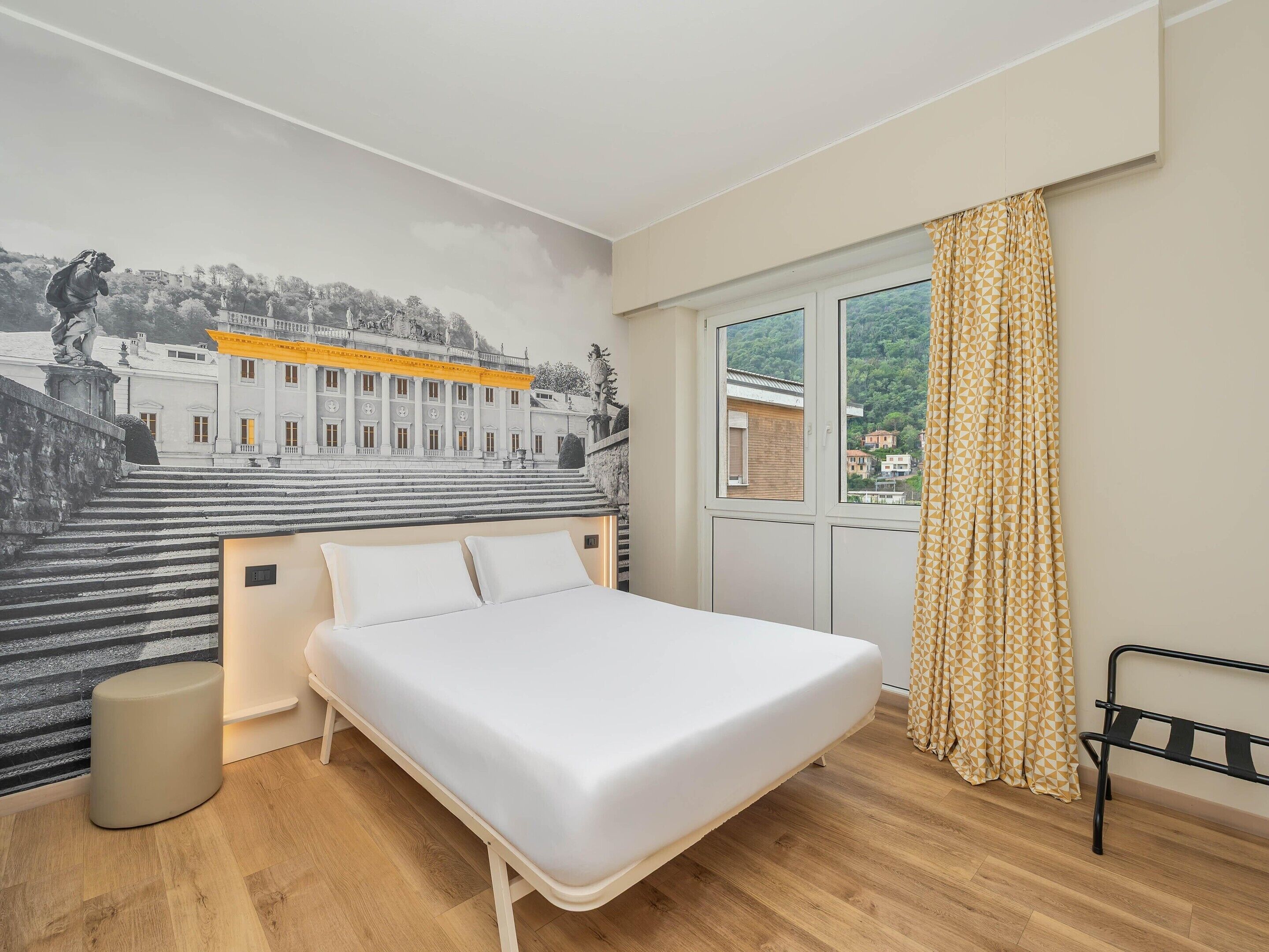 Ein Schlafzimmer mit einem Bett, einem Fenster mit Vorhängen, einer Wandklimaanlage und einem Wandbild eines Gebäudes.
