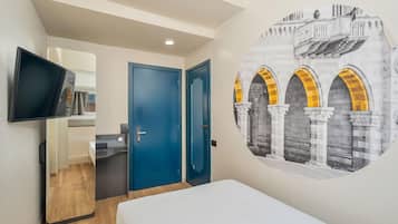 Habitación de hotel con una cama, un televisor fijado a la pared, una puerta y un mural arquitectónico.